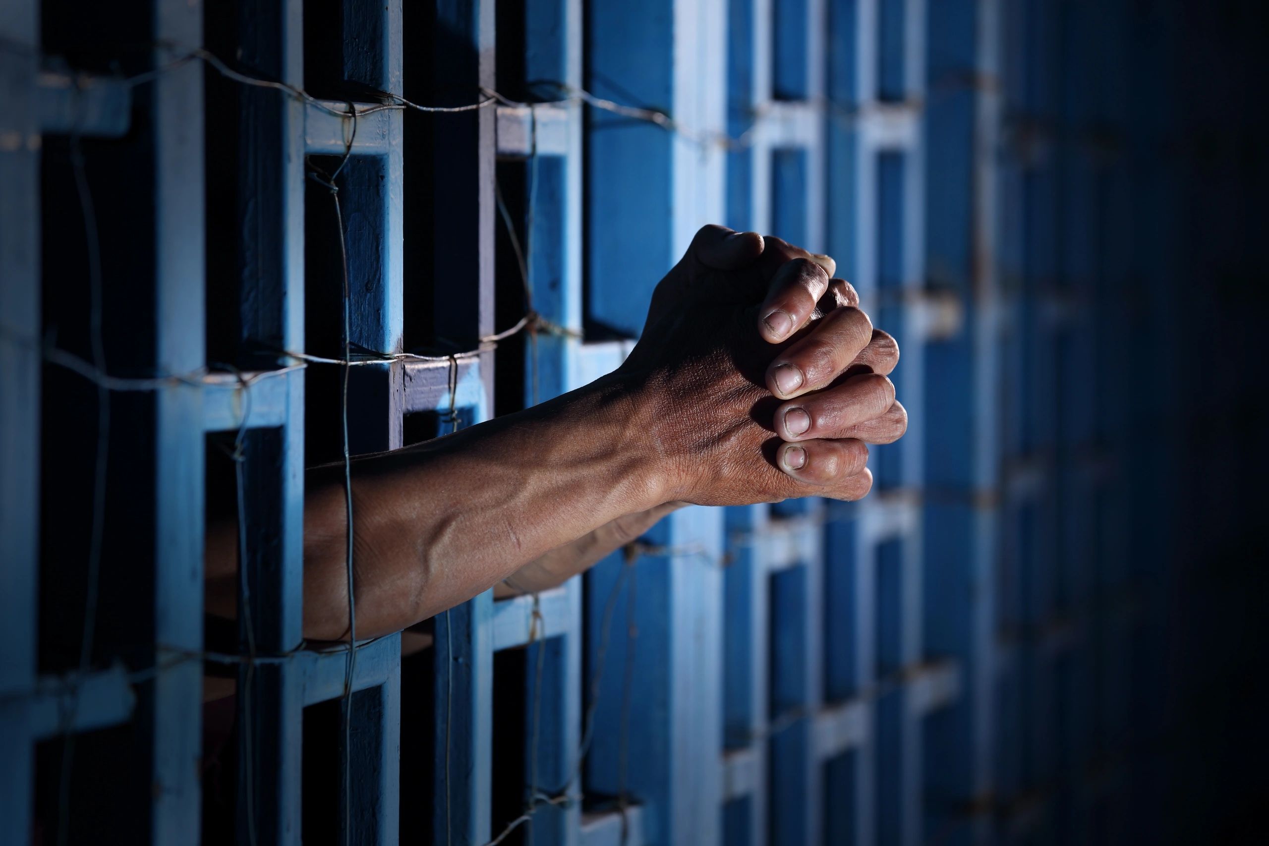 Hands clasped behind prison bars